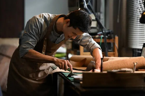 stock image Small business craftsman in apron carefully cutting piece of leather in his workshop.