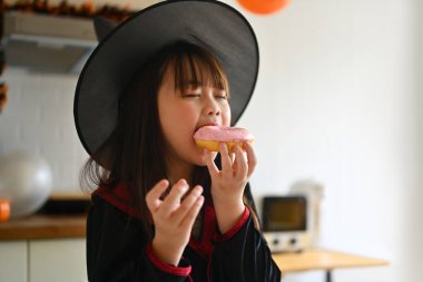 Cadılar Bayramı kutlamalarında tatlı çörek yiyen cadı kostümlü küçük tatlı kız..