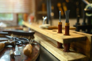 Kırsal atölyedeki ahşap masanın üzerinde panjurların arasından süzülen doğal ışık olan çeşitli deri el aletleri..