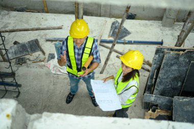 Güvenlik yeleği ve miğfer uzmanları inşaat alanındaki binanın yapısını tartışıyorlar..