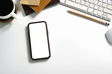 Üst görünüm boş ekranlı akıllı telefon, kahve fincanı ve ofis malzemeleri beyaz masada..