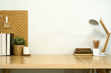 Kitapları, ev bitkisi ve lambası duvarda duran ahşap bir masa..