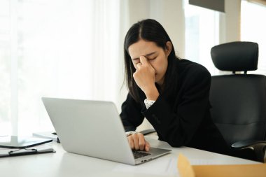 Ofiste dizüstü bilgisayarla çalışırken göz ağrısı çeken genç bir iş kadını..