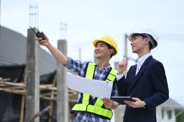 İki erkek inşaat işçisi tartışıyorlar ve yapıyı işaret ediyorlar..