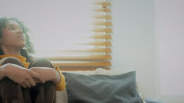 Düşünceli genç bir kadın. Kanepede oturmuş dizlerine sarılıyor. Çaresiz hissediyor..