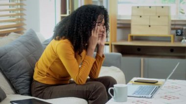 Oturma odasında kanepede oturan üzgün Afrikalı Amerikalı kadın dizüstü bilgisayarla çalışırken operasyonel sorunlar yaşıyor..