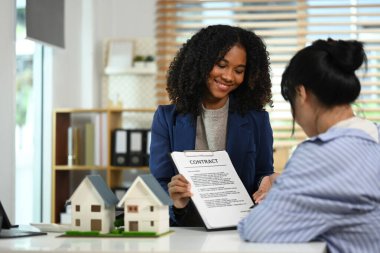 Dost canlısı bayan emlakçı müşteriye kontrat belgesini işaret ederek imza attı. Gayrimenkul ve emlak sigortası kavramları.