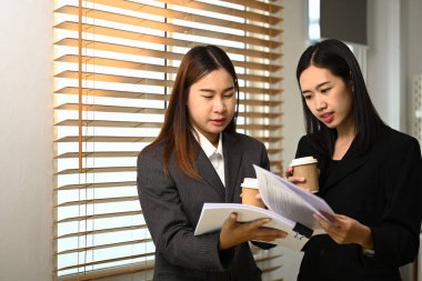 İki iş kadını pencerenin önünde durmuş, kahve molası sırasında öylesine tartışıyorlar..