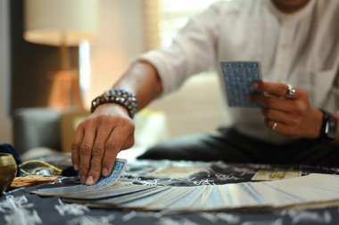 Bir insanın el tarot kartını mistik bir kumaşla kaplı bir masanın üzerinde rastgele seçerken görüntüsünü kapat..