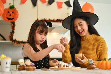 Anne ve kızı dekore edilmiş mutfakta Cadılar Bayramı kekleri dekore ediyorlar..