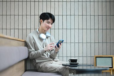 Modern kahve dükkanında oturan ve cep telefonlarını kontrol eden mutlu Asyalı genç adam..