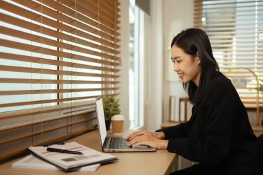 İş yerinde bilgisayarla çalışan gülümseyen Asyalı kadın çalışanın yan görüntüsü.