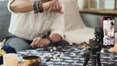 Falcı akıllı telefonlu blog için video kaydedilirken masaya kabuk dökme ve dağıtma büyüsü yapıyor.
