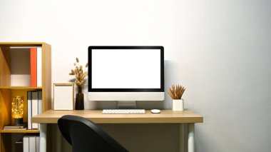 Minimalist ev ofisi, boş ekranlı bilgisayar monitörü ve beyaz duvara yakın ahşap kitaplık..