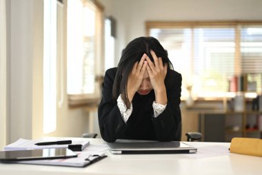 Ofis masasında oturan genç bir iş kadını, kafası ellerinin arasında, stresli ya da bunalmış görünüyor..