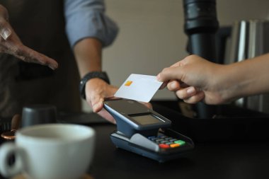 Modern kahve dükkanının temassız ödeme terminalinde müşterinin kredi kartına dokunuşunu kapat..