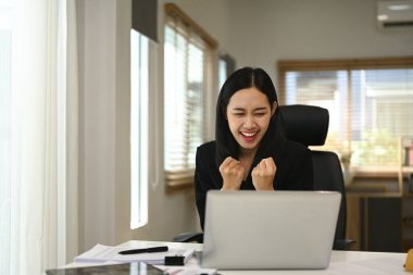 Heyecanlı genç iş kadını laptopta iyi haberler okurken başarısını kutluyor..