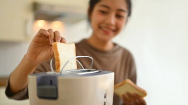 Mutfakta kahvaltı hazırlayan, tost makinesine ekmek koyan mutlu genç kadın..