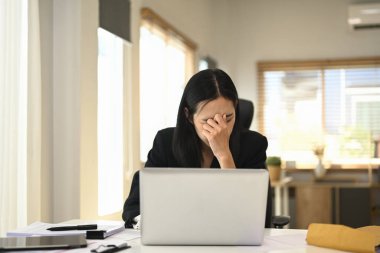 Çalışırken masasında oturan yorgun genç bir iş kadını..