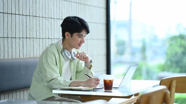 Kafe masasında dizüstü bilgisayarla çalışan günlük kıyafetli genç adam..