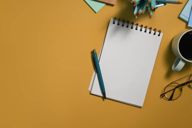 Boş not defteri, kalem, bardak ve kahve. Sarı arka planda fotokopi alanı var..