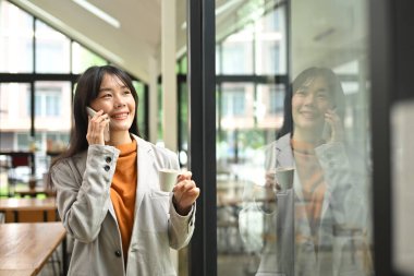Çekici genç iş kadını ofis penceresinin yanında dururken hoş bir telefon konuşması yapıyor..