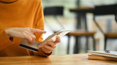 Kredi kartı tutan ve akıllı telefonuyla online ödeme yapan genç bir kadın. Kapat..