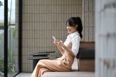 Kahve dükkanında otururken akıllı telefondan mesaj okuyan genç bir kadın..