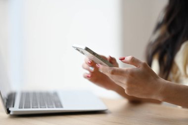 Genç bir kadın elinde bir cep telefonu tutarken elinde bir dizüstü bilgisayarla oturuyor..
