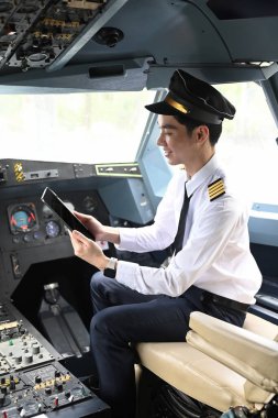 Pilot bir uçağın kokpitinde oturuyor ve dijital tablet kullanıyor..