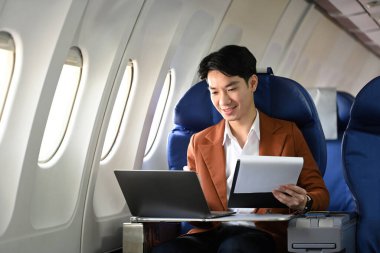 Profesyonel iş adamı uçakla seyahat ediyor ve laptopuyla çalışıyor. İş seyahati ve ulaşım kavramı.