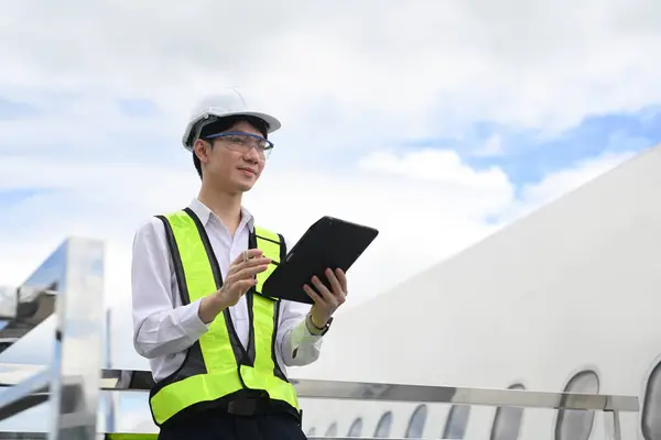 Stock image Professional aviation engineer using digital tablet while standing on staircase or platform near the aircraft.