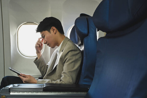 Перегруженный работой и напряженный молодой бизнесмен с головой в руках, сидящий в кресле самолета.