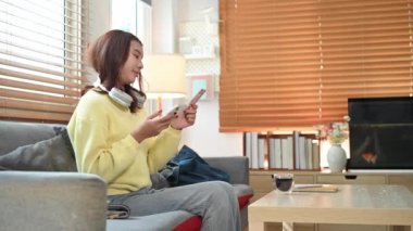 Gülümseyen genç Asyalı kadın kredi kartı tutuyor ve online alışveriş için cep telefonu kullanıyor..