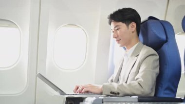 Uçak koltuğunda oturan ve dizüstü bilgisayarıyla çalışan çekici bir iş adamı. İş seyahati kavramı.