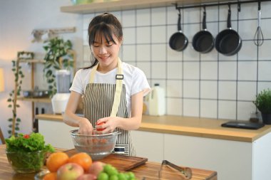 Önlüklü güzel bir kadın ahşap tezgahta taze malzemelerle sağlıklı bir yemek hazırlıyor..