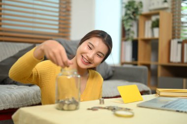 Cam kavanoza bozuk para atan mutlu genç bir kadın. Finansal planlama, bütçe veya tasarruf kavramı.