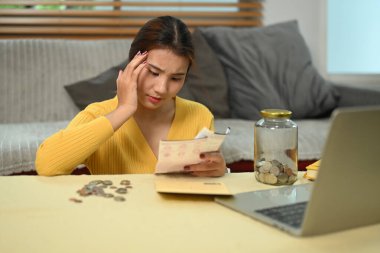 Oturma odasında otururken masrafları yöneten ve kişisel bütçe planlayan stresli genç bir kadın..