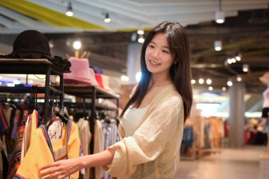 Hafif giyinmiş genç bir kadın, sıradan bir kıyafet mağazasında alışveriş yapıyor..