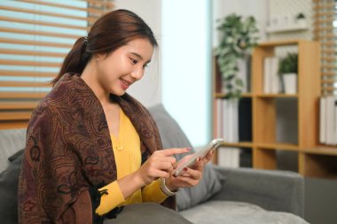 Gülümseyen genç bir kadın cep telefonundaki sosyal medya uygulamasında mesaj ve kaydırma haberleri yolluyor..