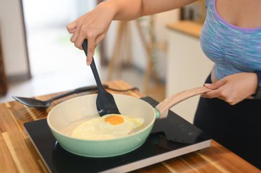 Hareketli genç bir kadının yakın plan görüntüsü ev mutfağında kahvaltıda kızarmış yumurta giyer..