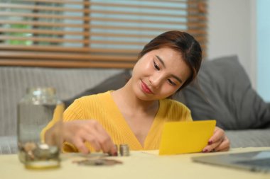 Neşeli genç bir kadın para sayıyor ve masaya para yığıyor. Tasarruf ve mali sorumluluk kavramı.