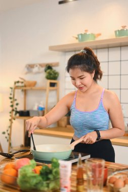 Genç bir kadın sobanın üstünde malzemelerini karıştırıyor, modern bir mutfakta sağlıklı bir yemek hazırlıyor..