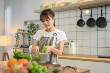 Gülümseyen genç kadın, mutfak tezgahında taze ürünlerle yemek hazırlıyor..