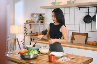 Güzel genç bir kadın, taze sebzeler ve mutfak gereçleri ile tavada malzemeleri karıştırıyor..