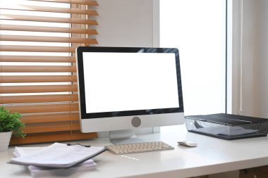 Çalışma masasında beyaz boş ekran bilgisayar monitörü, evrak ve ev bitkisi.