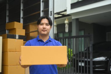 Paketlerle dolu bir kamyonun yanında duran karton kutu taşıyan yakışıklı teslimatçı..