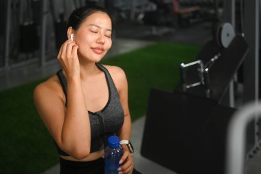 Spor salonunda dinlenirken kulaklıkla müzik dinleyen güzel bir atlet kadın..