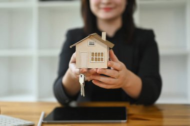 Kendine güvenen bir emlakçı, elinde anahtarla model bir ev tutuyor. Gayrimenkul değerlendirmesi ve emlak kavramı.