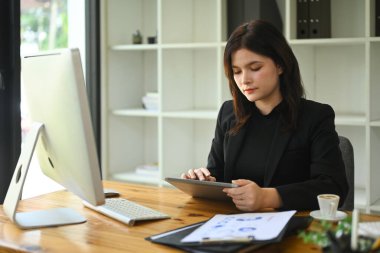 Ofis masasında dijital tablet kullanan siyah takım elbiseli profesyonel bir iş kadını..